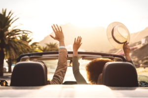 A couple in a convertible facing the sun with a palm tree on the side. This is USVI, this article is about how to find the cheapest rental cars in the US Virgin Islands