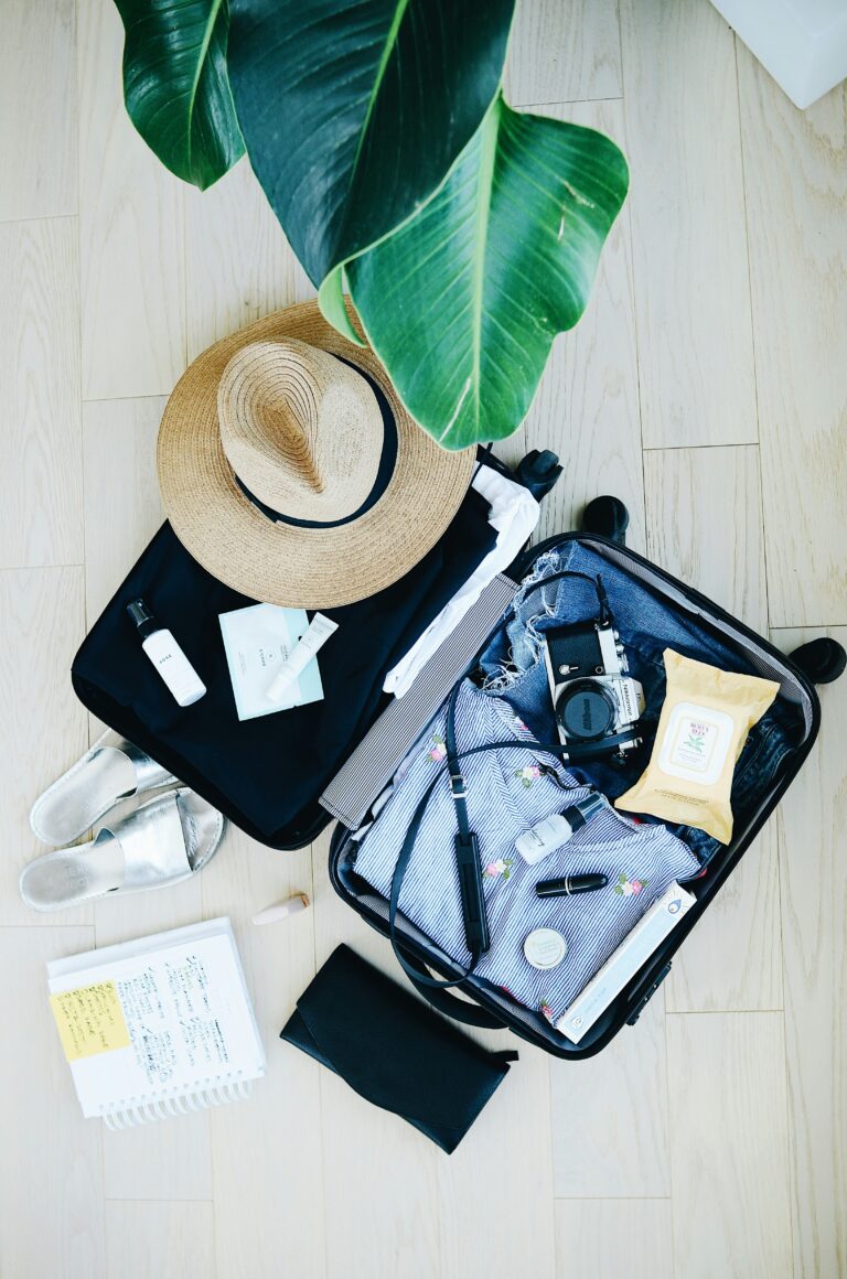An open suitcase packed for a trip with clothes, a camera, a journal, and other personal items.